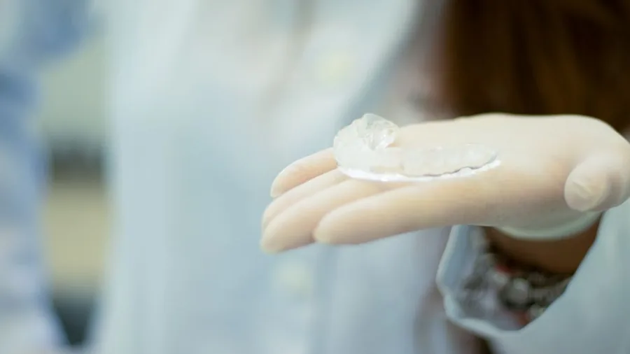 장갑 낀 손에 올려둔 투명한 치아 보호 장치